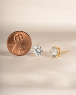 Dainty earrings on a neutral background being compared to the size of a penny 