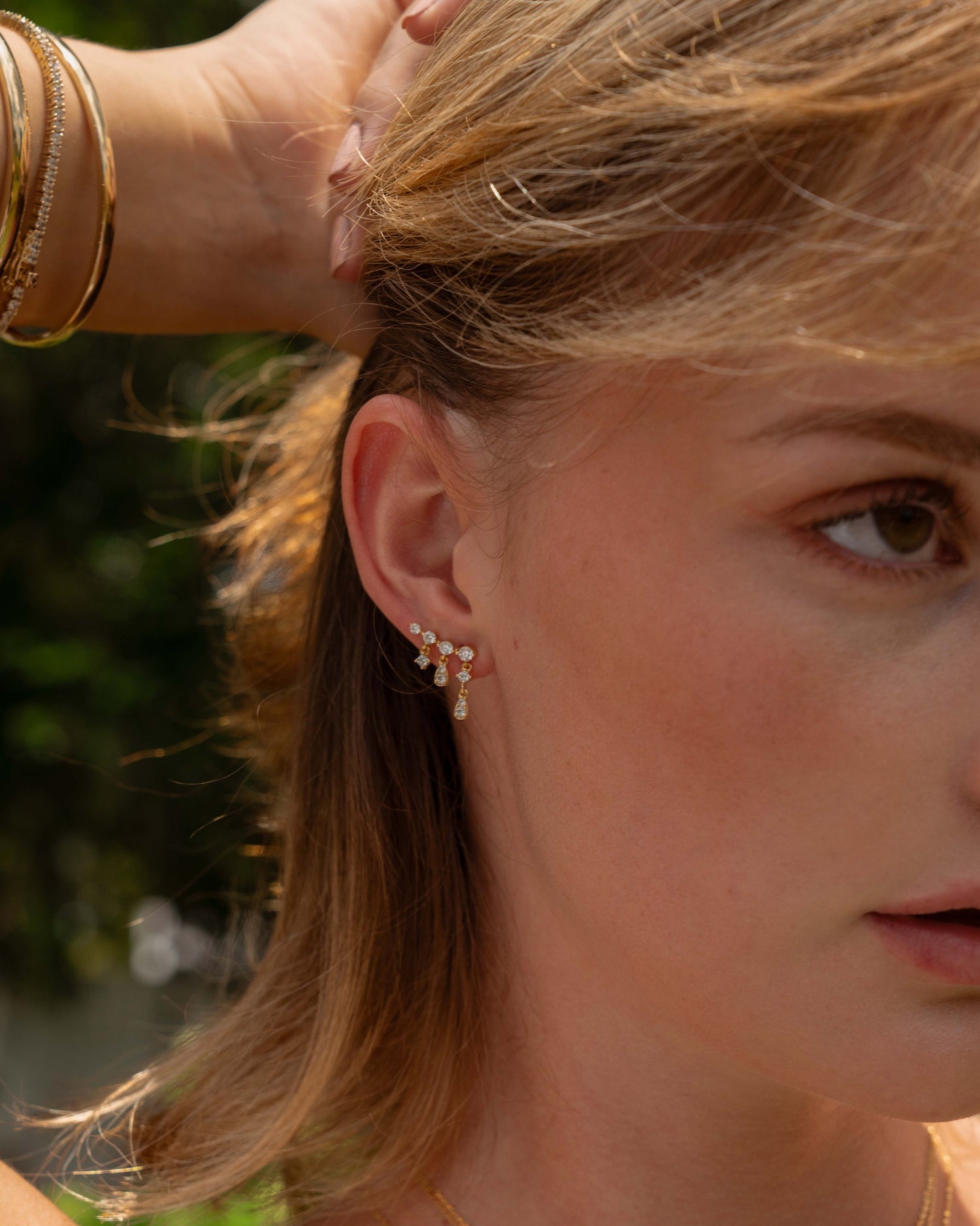 Model wearing gold dangling earring with cubic zirconia stones