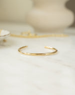 Closeup image of gold bangle bracelet on white marble table