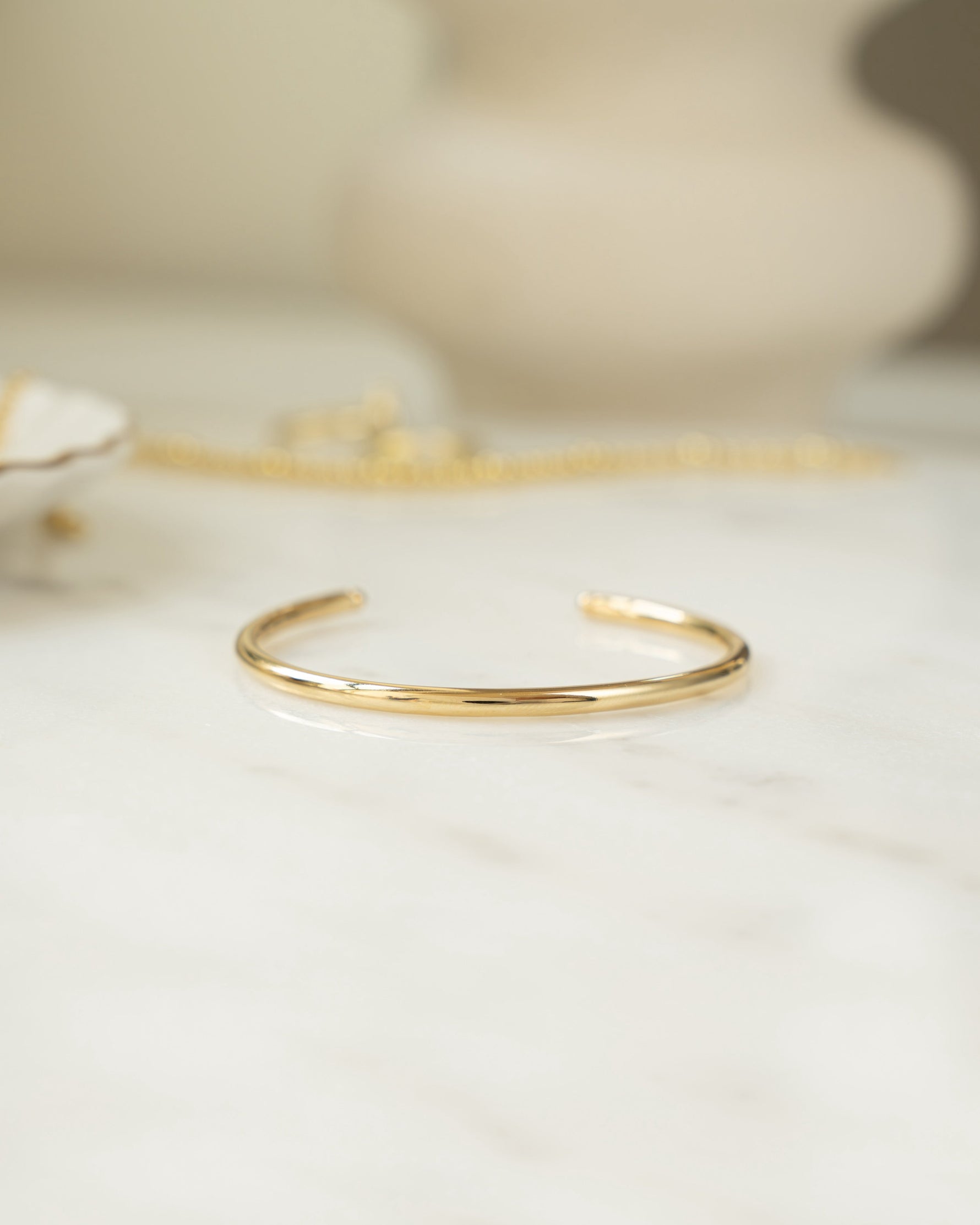 Closeup image of gold bangle bracelet on white marble table