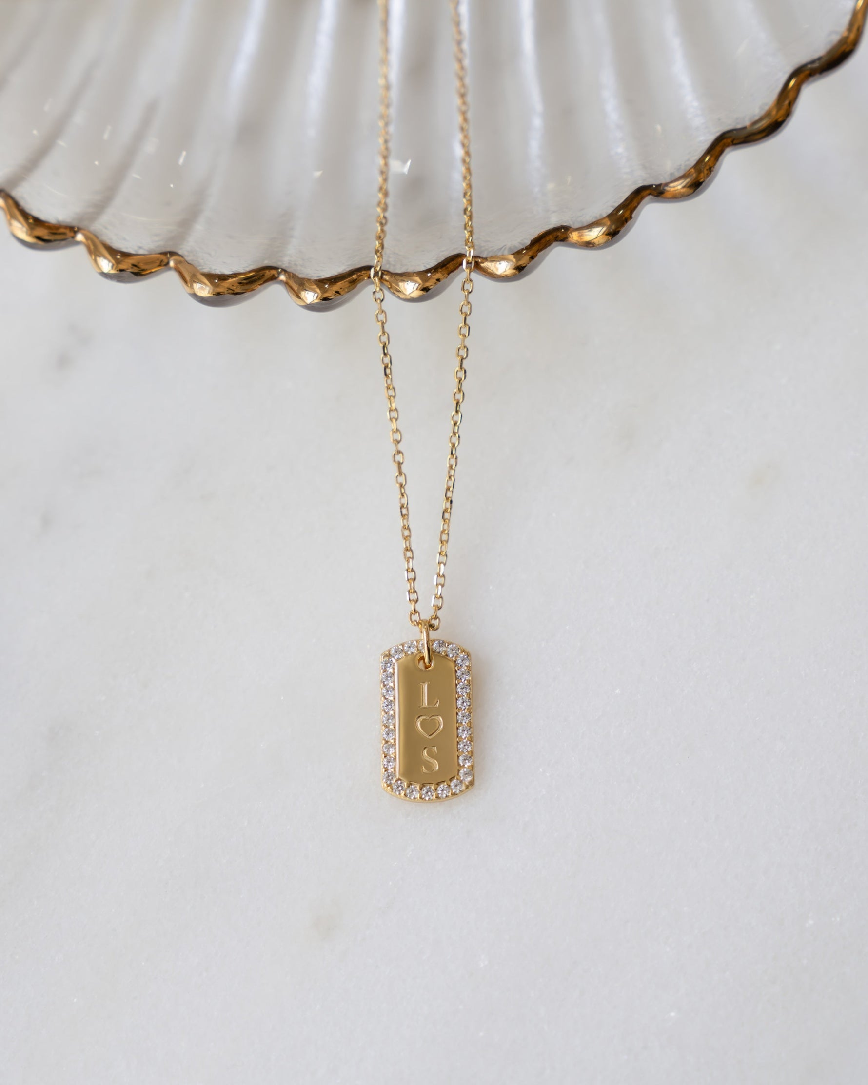 flatlay image of gold dog tag necklace with pavé cubic zirconia stones