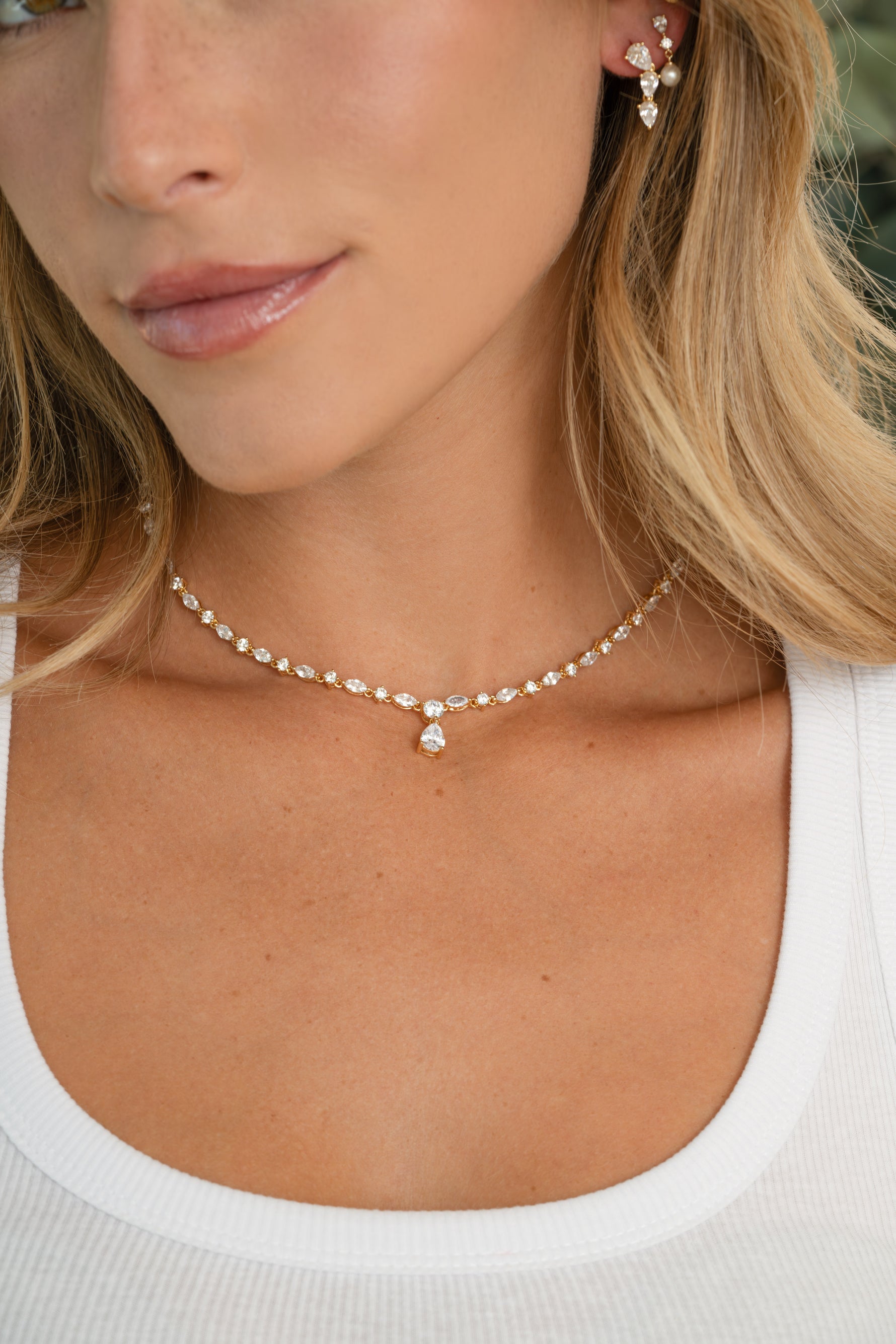 Model wearing gold diamond pendant tennis necklace and matching pear shaped diamond earrings
