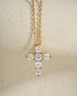 Gold cross pendant necklace with cubic zirconia diamonds on a beige background