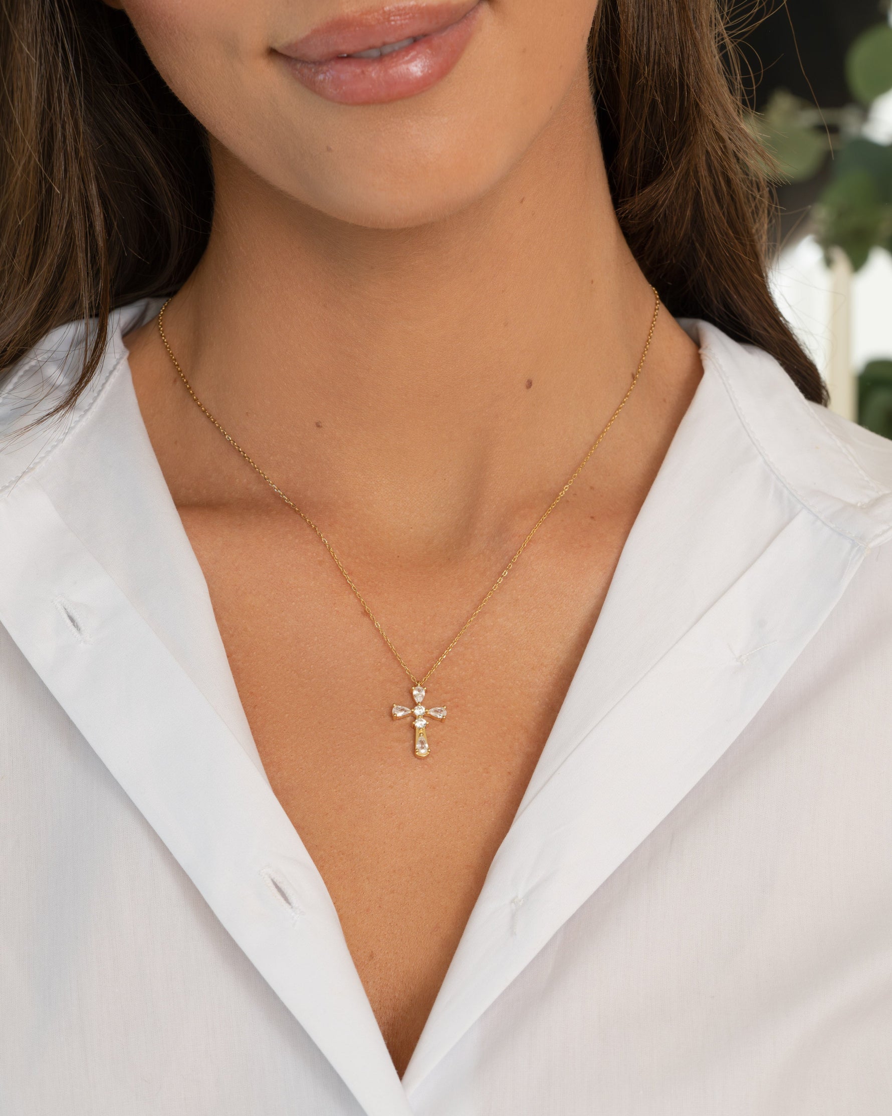 Close-up of a person wearing a gold necklace with a cross pendant on a white shirt.