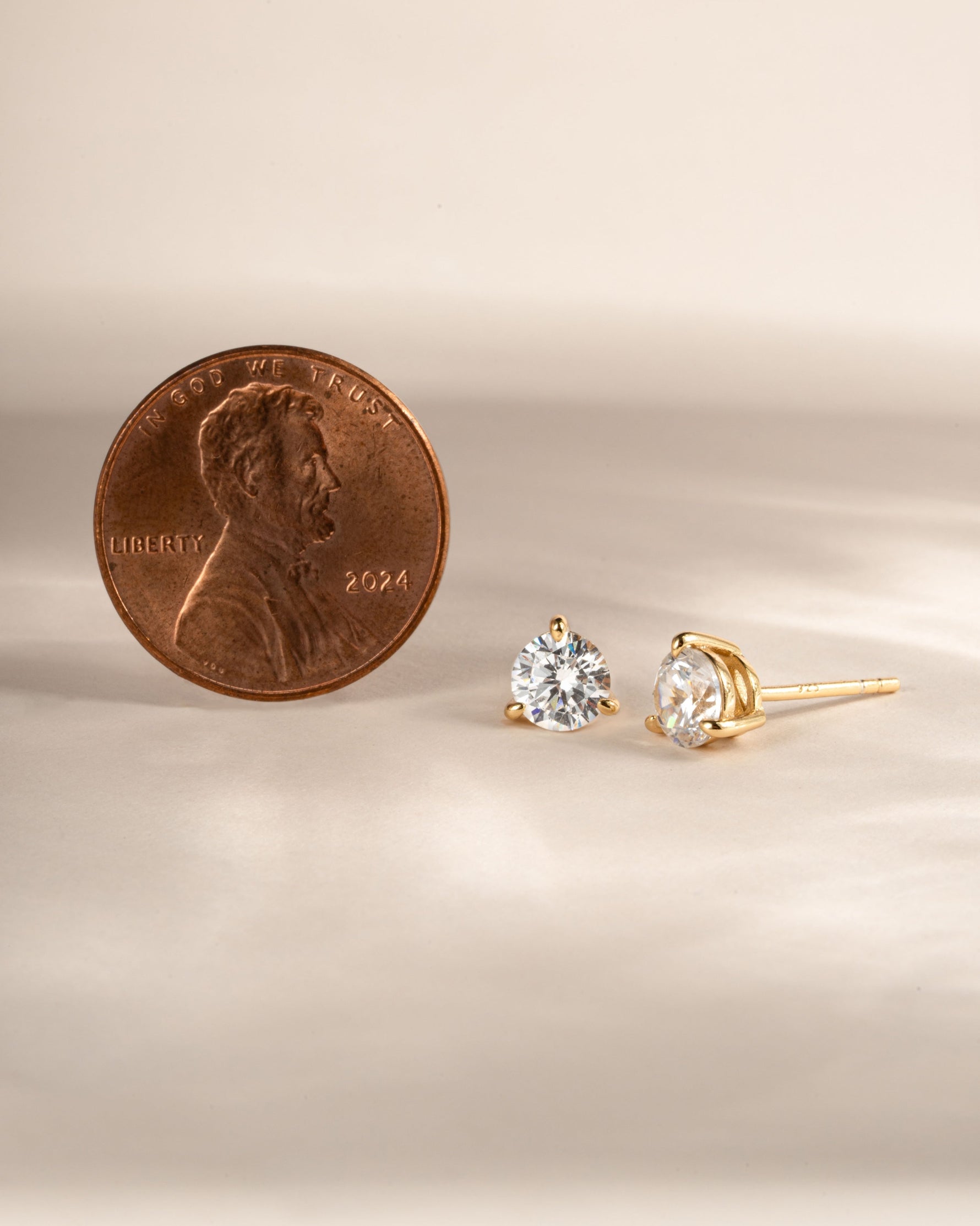 Gold minimalist stud earrings next to a penny on a beige background