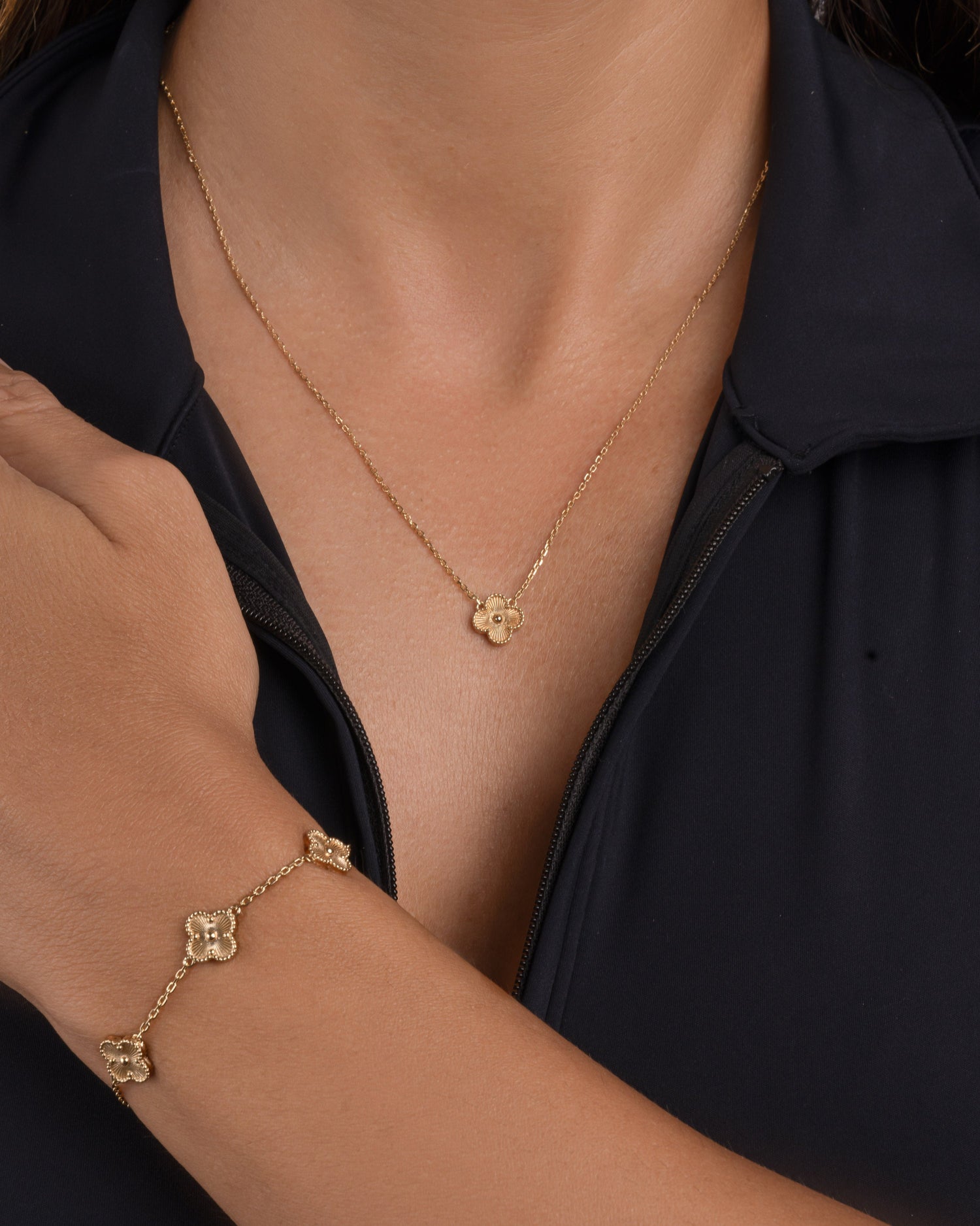 Gold clover necklace and gold clover charm bracelet on a person wearing a black top