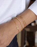 Model wearing gold bracelet stack featuring a bracelet set, a diamond tennis bracelet and a religious jewelry piece with a cross pendant on a gold chain
