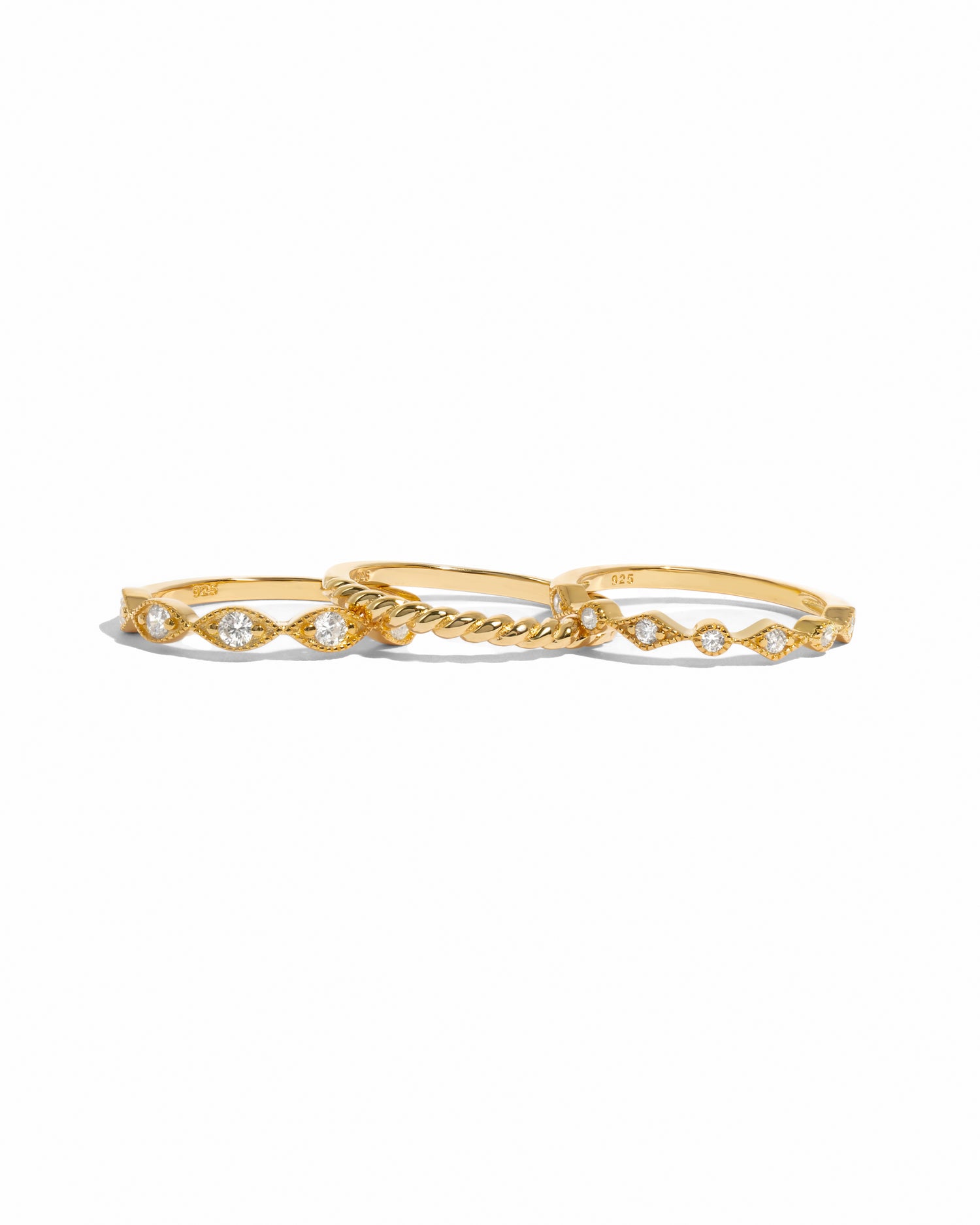 A gold ring set with three dainty rings and intricate textured designs on a white background