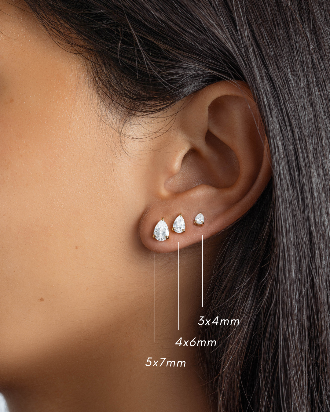 Gold stud dainty earrings with a pear cut cubic zirconia stones featuring a 5x7mm diamond studs, a 4x6mm minimalist stud earrings and a 3x4m pear cut small earrings on models ear