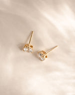 Gold earrings with clear gemstones on a light beige background