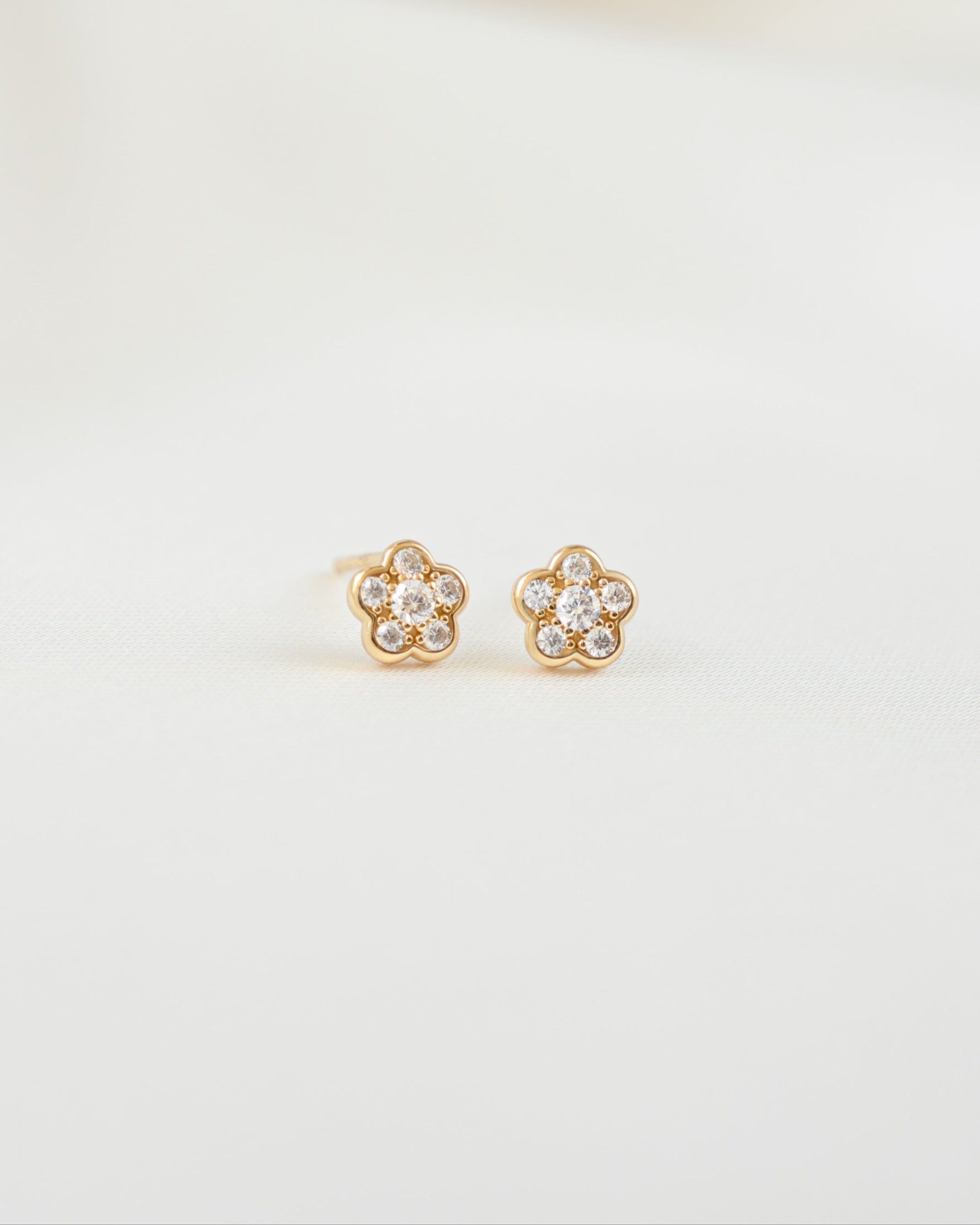Gold cubic zirconia earrings with a flower earring design on a plain background
