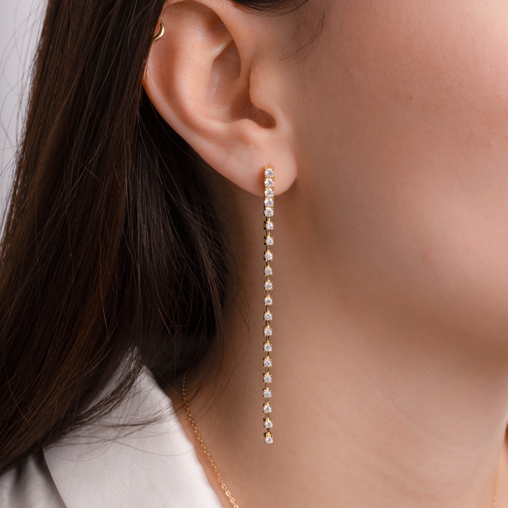 model wearing gold drop earrings with cubic zirconia stones.