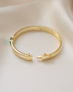 Side view of gold gemstone bracelet with emerald birthstone on a beige fabric background
