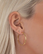 Model wearing 32mm gold hoop earrings, styled with bezel and ball stud earrings in second and third piercings.