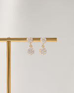 Pair of gold flower earrings with a diamond charm on a gold stand against a light gray background
