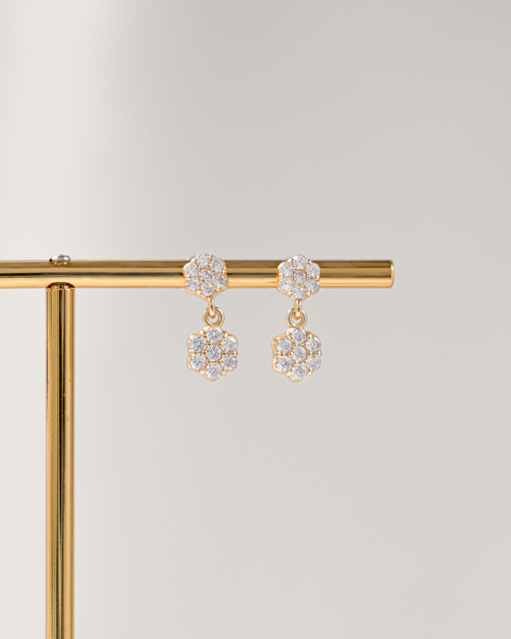 Pair of gold flower earrings with a diamond charm on a gold stand against a light gray background