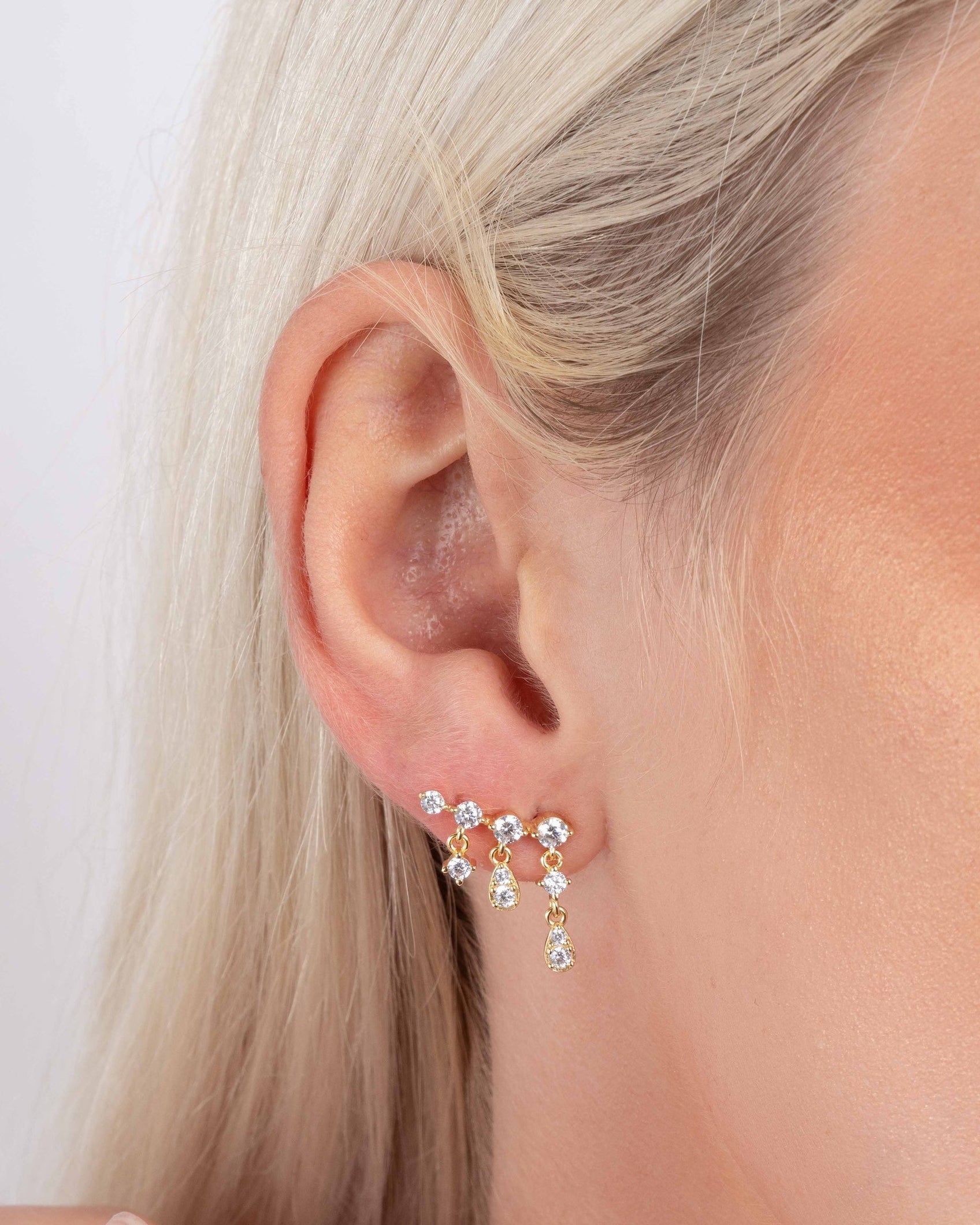 Close up of models ear wearing cubic zirconia gold diamond earrings with an ear climber design 