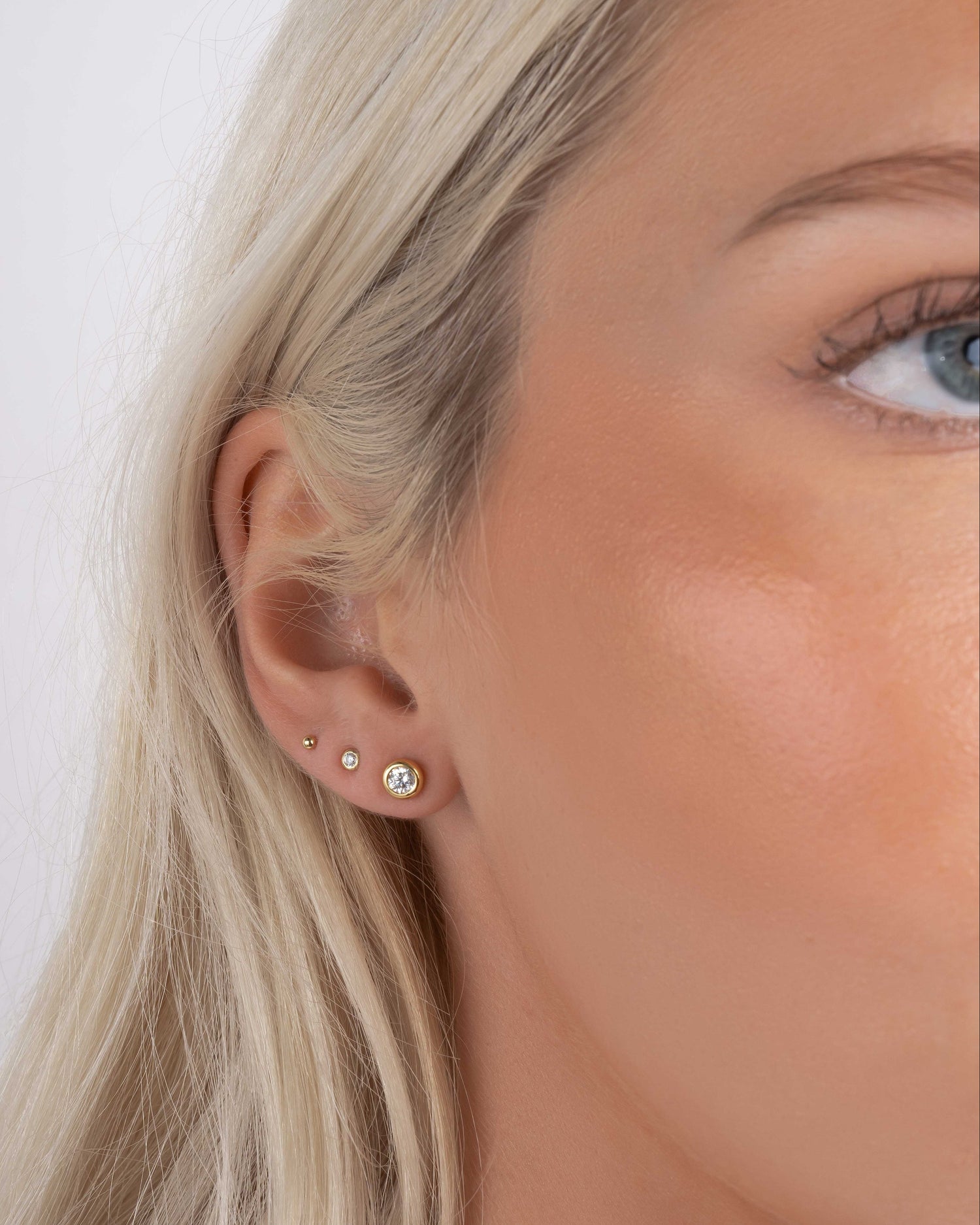 Closeup of models ear wearing gold plated earrings featuring diamond stud earrings, tiny earrings and a gold ball stud earring