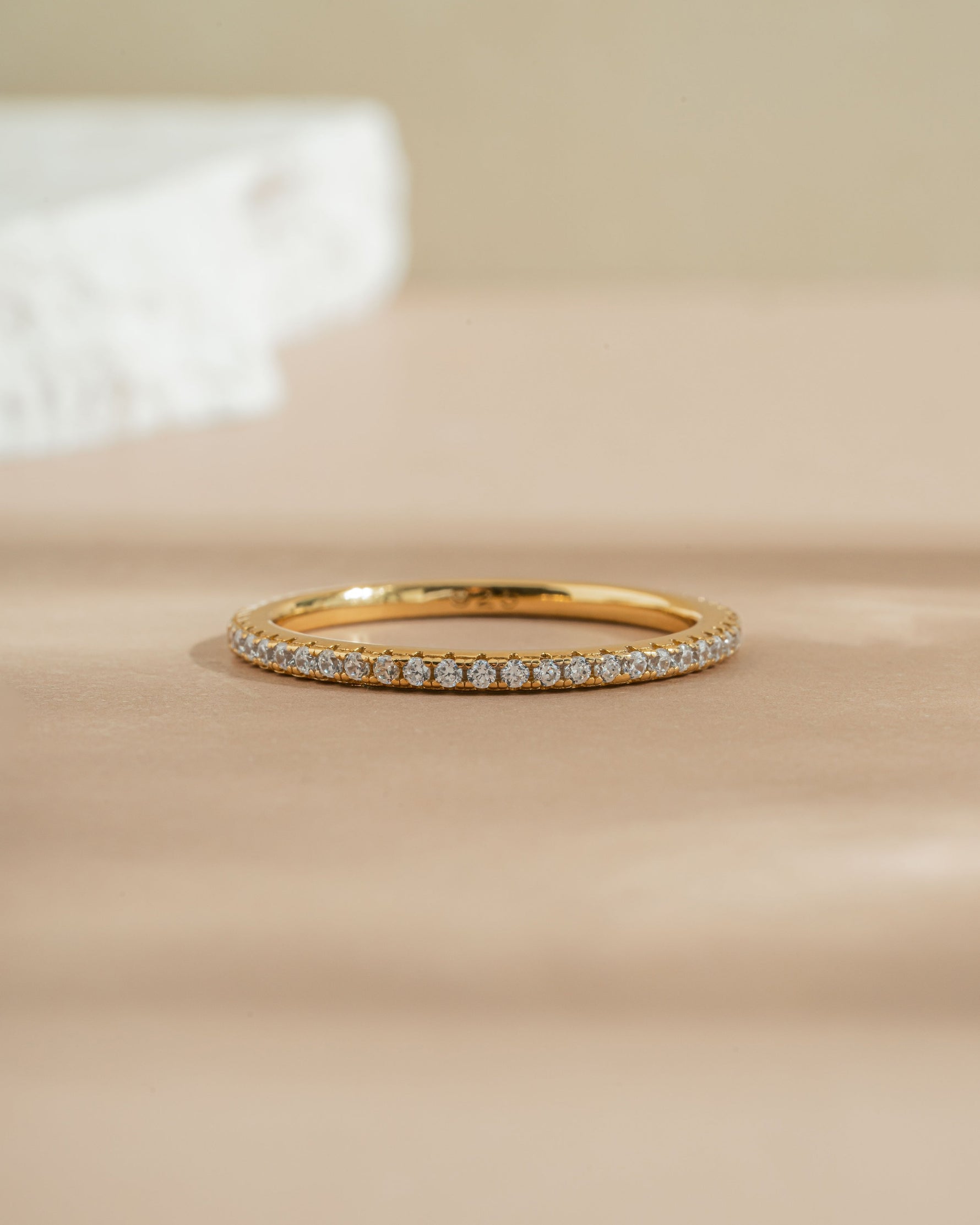 Gold diamond stacking ring on a beige surface