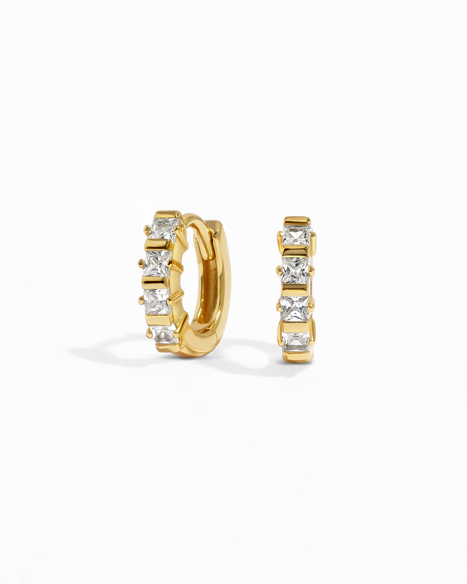 A pair of gold studded huggie earrings with cubic zirconia stones, displayed against a white background.
