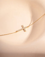 Gold adjustable bracelet with a cross diamond pendant on a white background