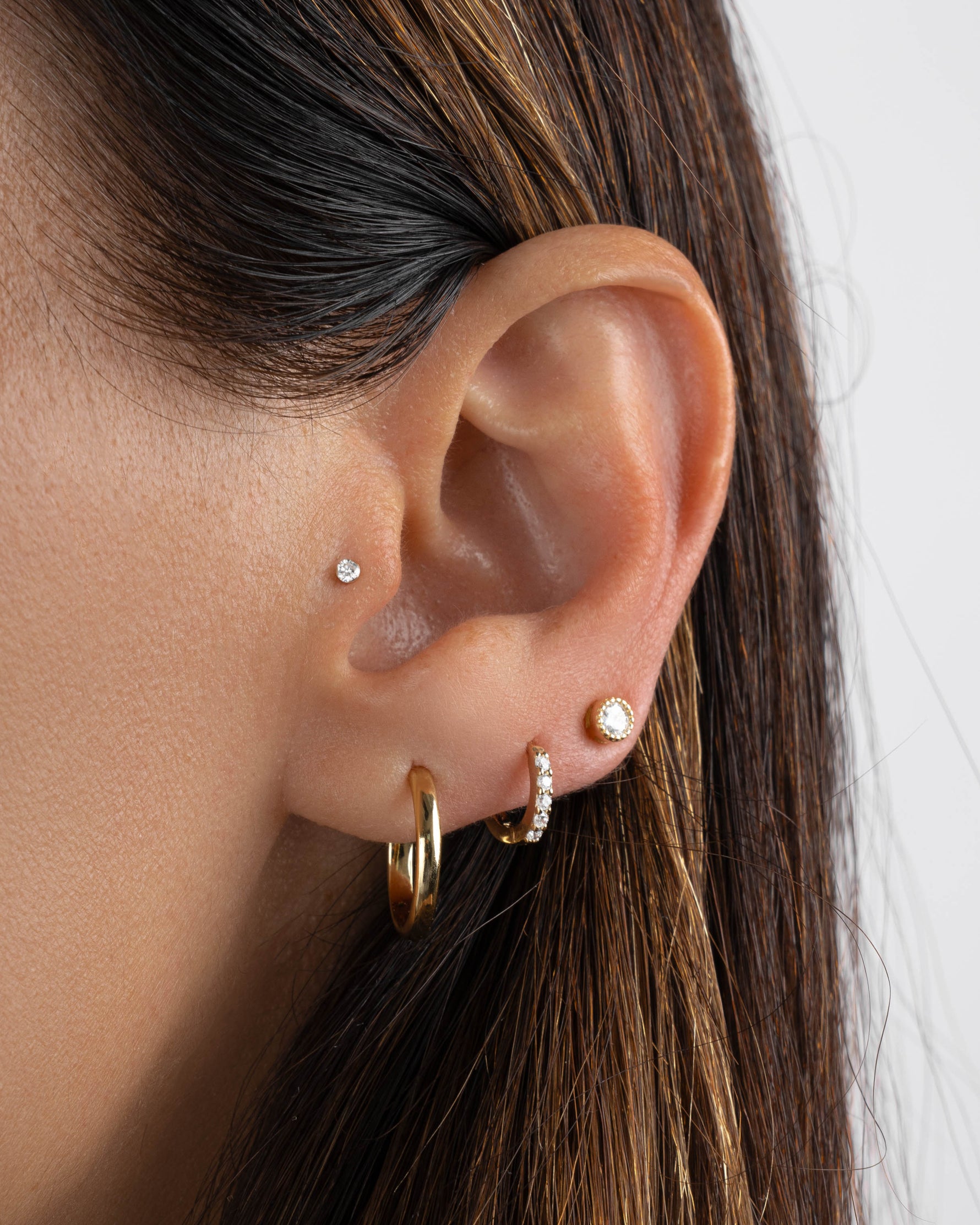 Close-up of an ear with multiple earrings featuring a gold hoop earring, a huggie hoop, and a diamond stud earring
