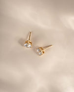 Gold earrings with cubic zirconia gemstones on a beige background