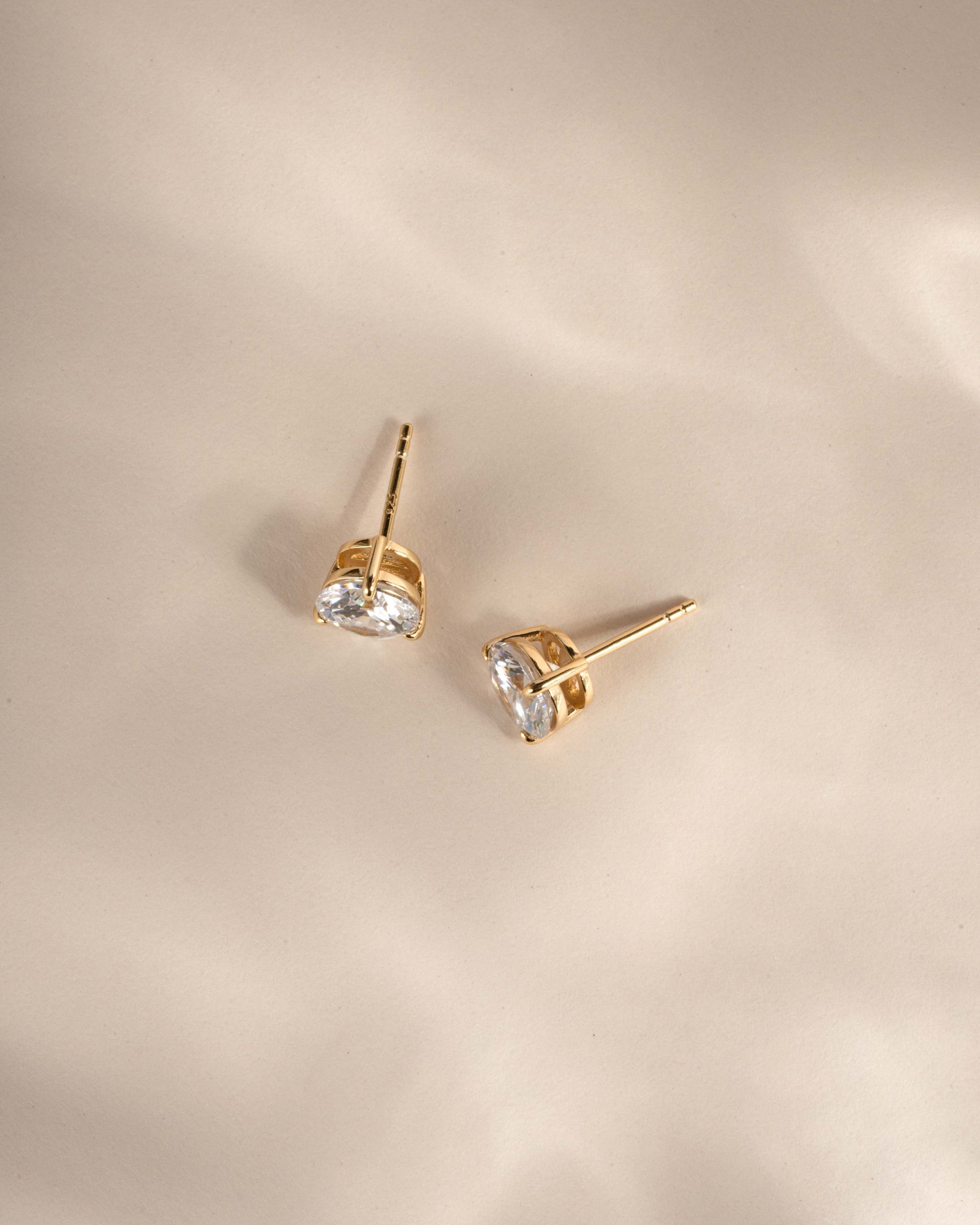 Gold earrings with cubic zirconia gemstones on a beige background