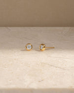 Gold stud earrings on a beige surface with a neutral background