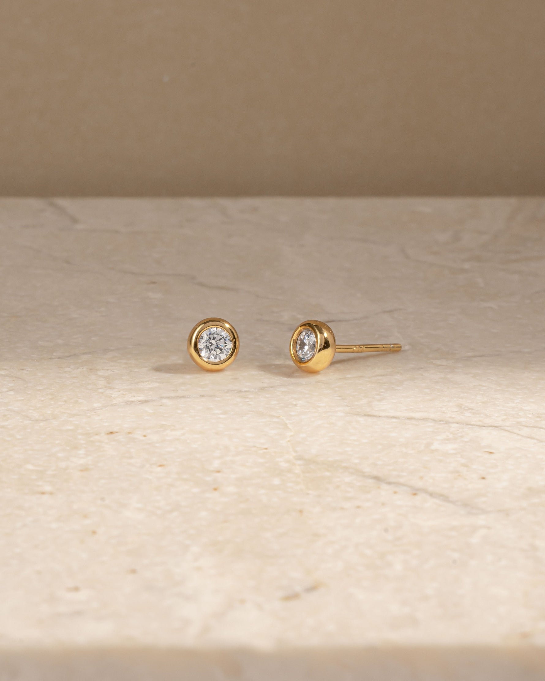 Gold stud earrings on a beige surface with a neutral background