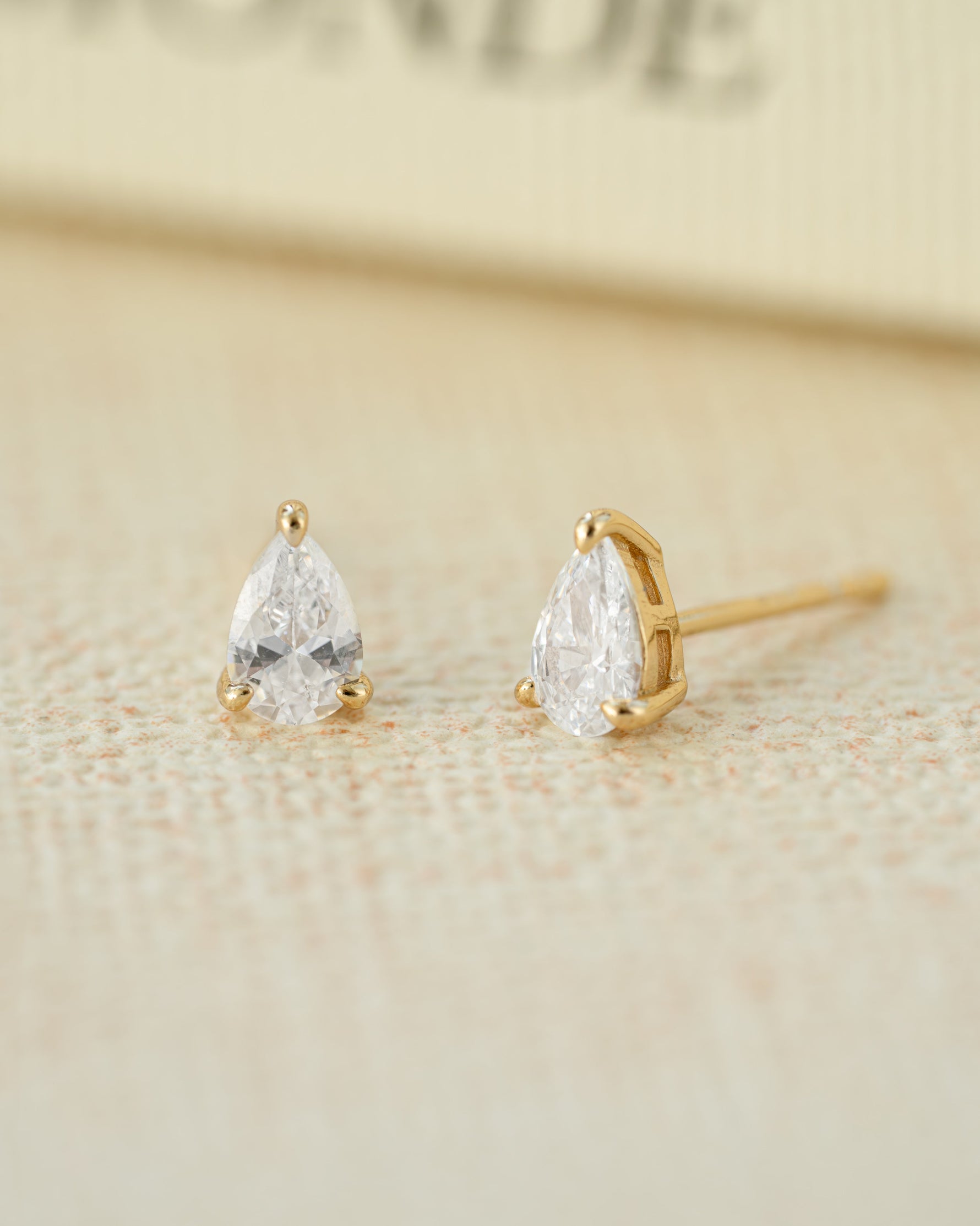 Gold teardrop earrings on a beige background