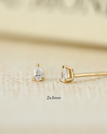 Gold earrings with pear-shaped gemstones on a beige background