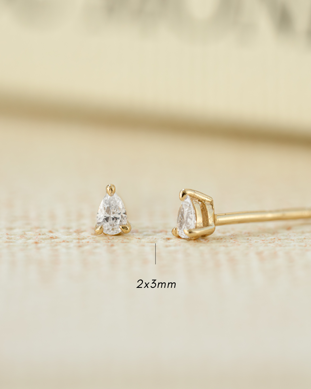 Gold earrings with pear-shaped gemstones on a beige background