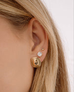 Model wearing oval statement earrings, round solitaire stud earrings, and diamond bezel stud earrings on model