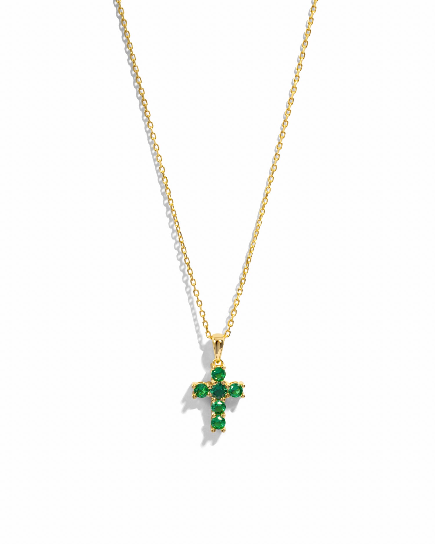 Gold cross necklace with green gemstones on a white background