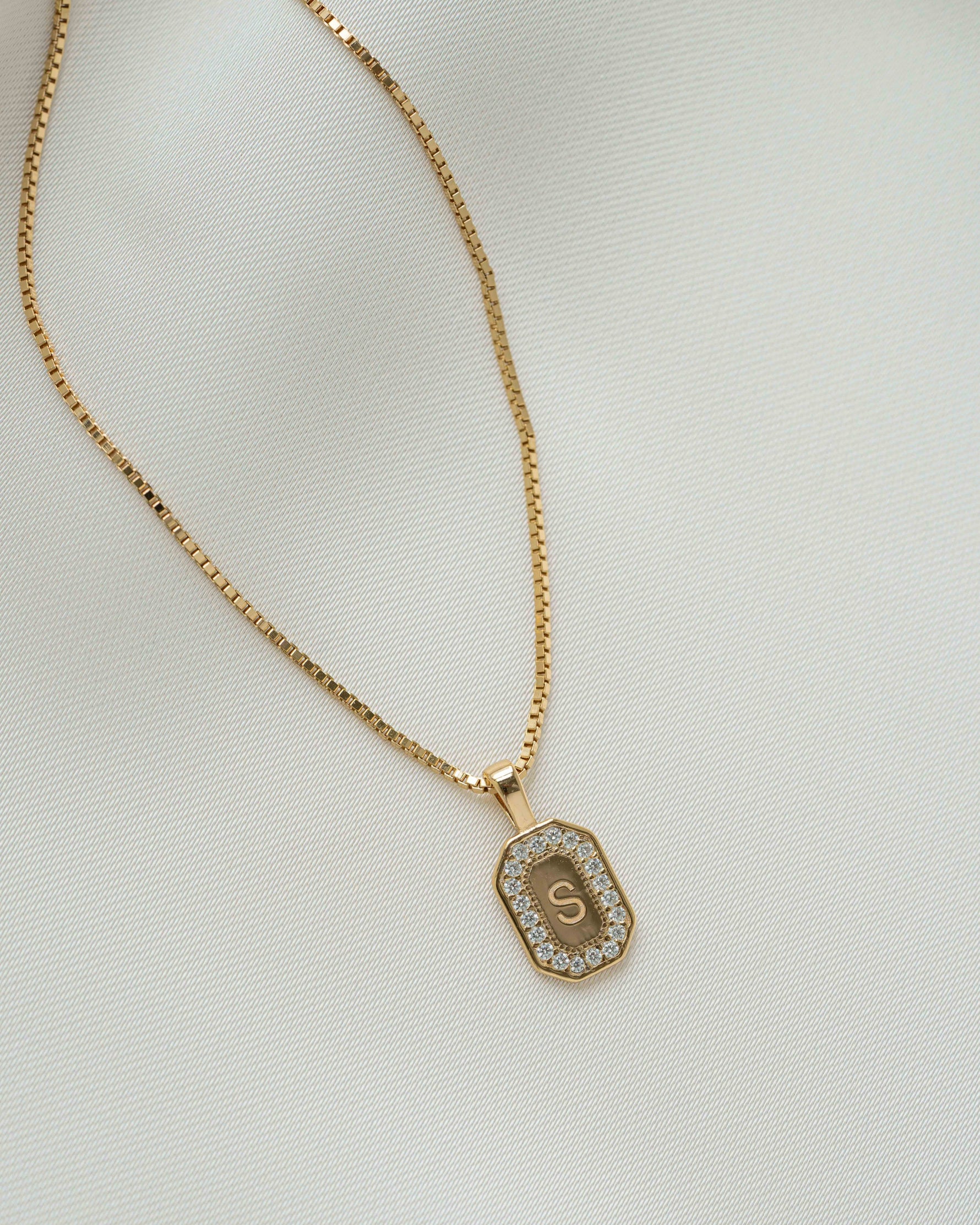 Gold chain custom necklace with a custom pendant "S" on a plain background 