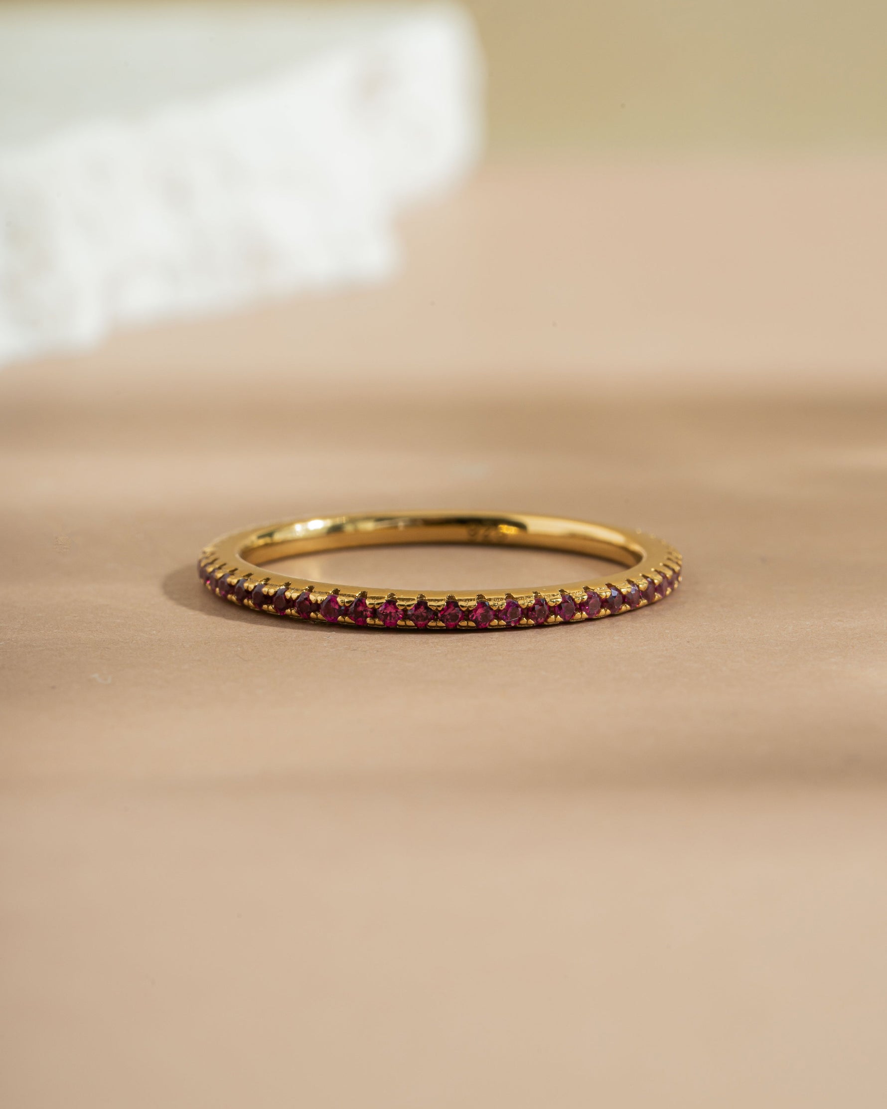 Gold ruby eternity ring band on a biege surface