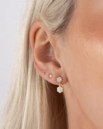 Close-up of a person wearing gold dangle earrings with a floral earring design and diamond stud earrings