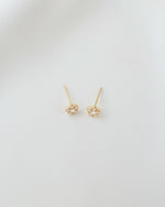 A pair of gold minimalist cubic zirconia stud earrings on a plain background