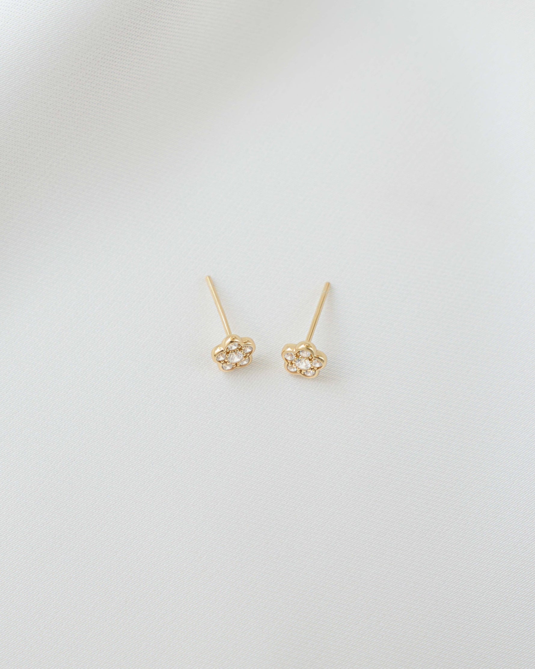 A pair of gold minimalist cubic zirconia stud earrings on a plain background
