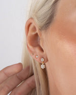 Model wearing gold dainty earrings with a drop earring design, a gold stud earring in her second hole and a ball stud earring in her third hole