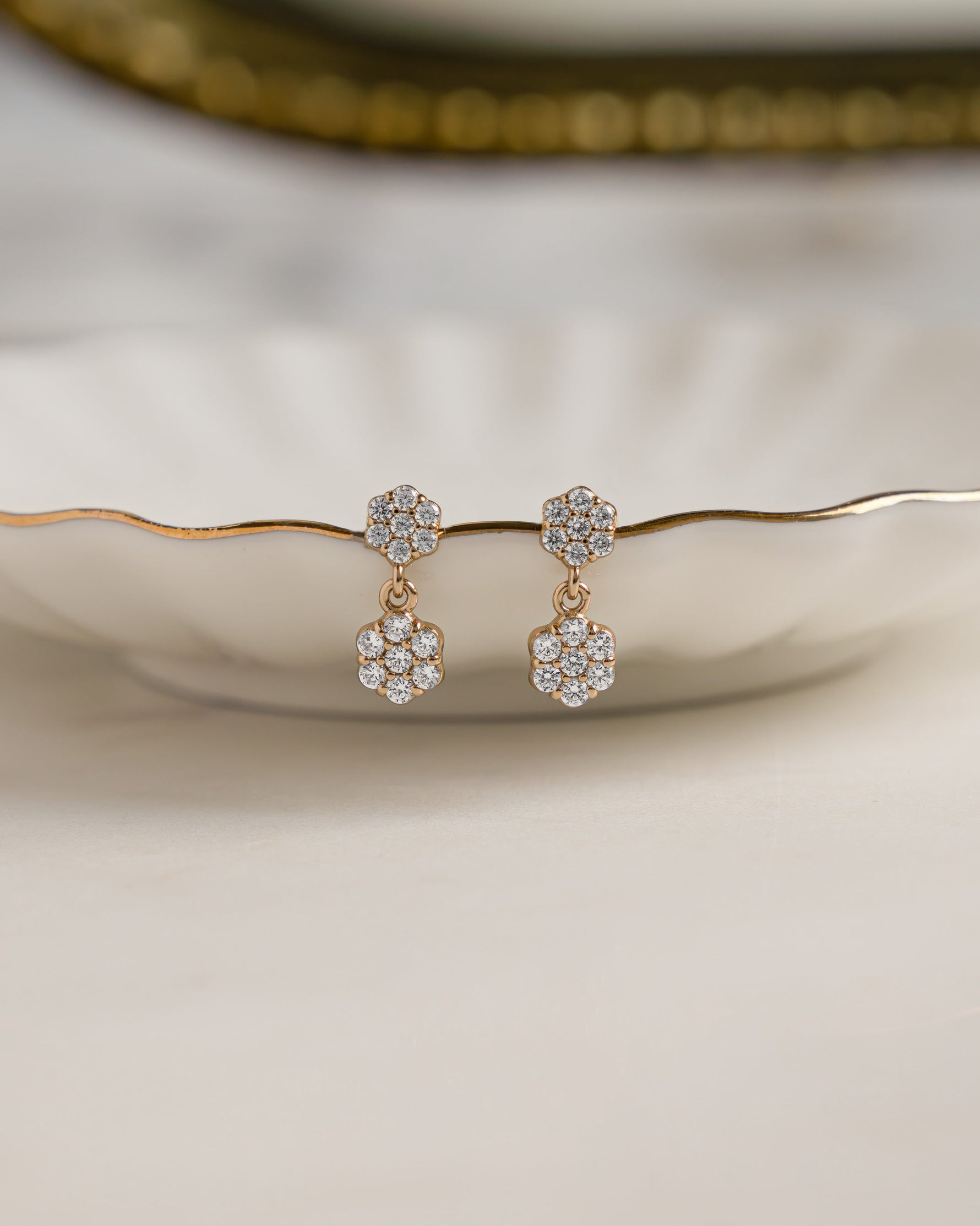 Pair of gold small stud earrings with clear stones on a decorative plate.