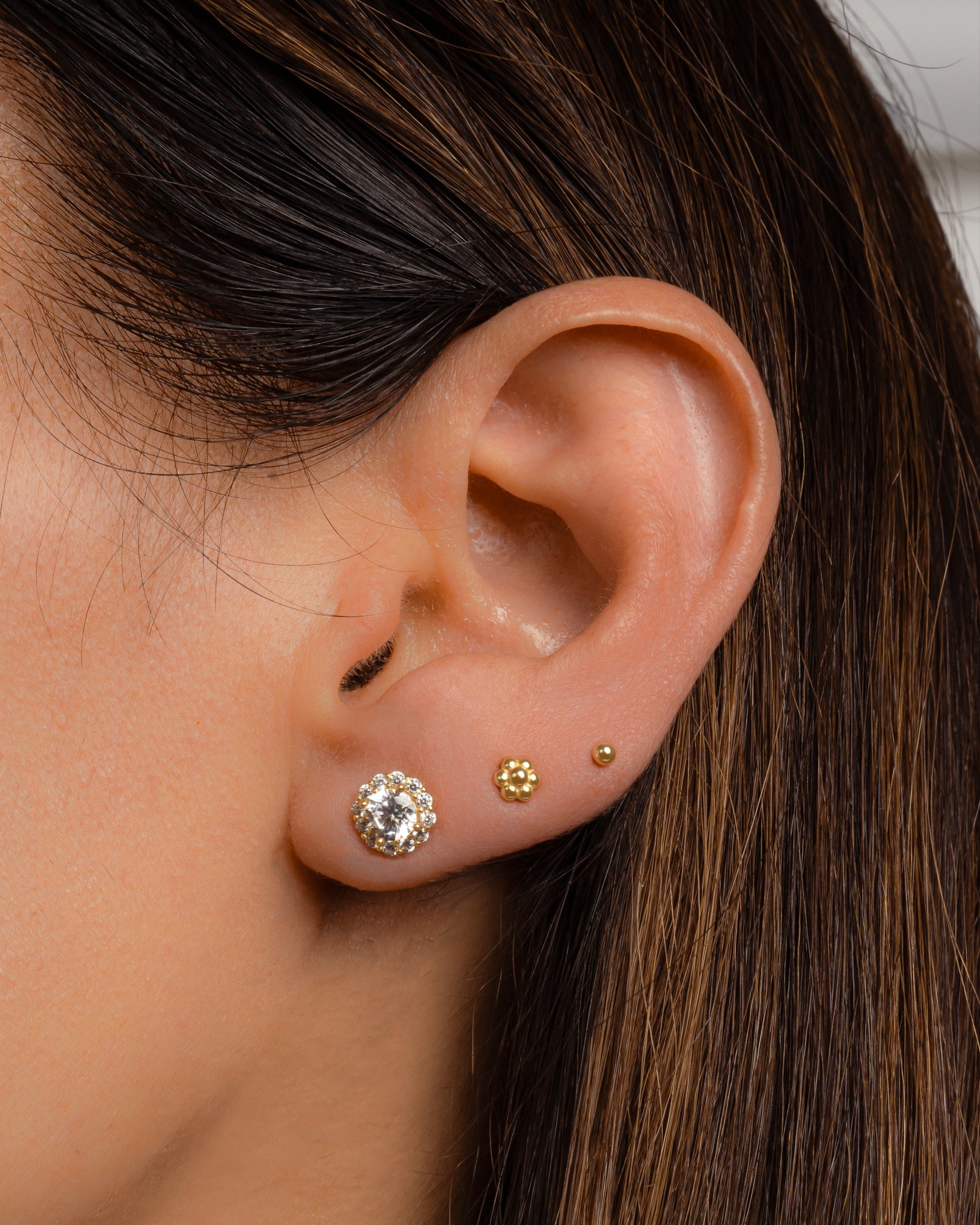 A model's ear with diamond halo and gold tiny flower studs.