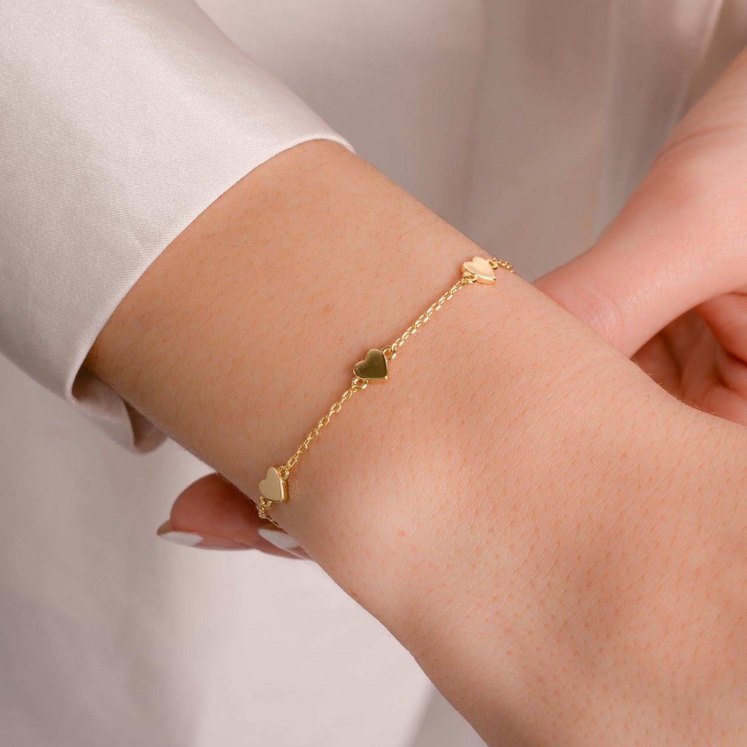 A love heart bracelet in shiny gold, styled on a wrist, adding a minimalist look to a casual outfit. 