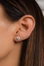 Model wearing gold halo stud earrings, a dainty gold flower stud earring, and a small ball stud earring