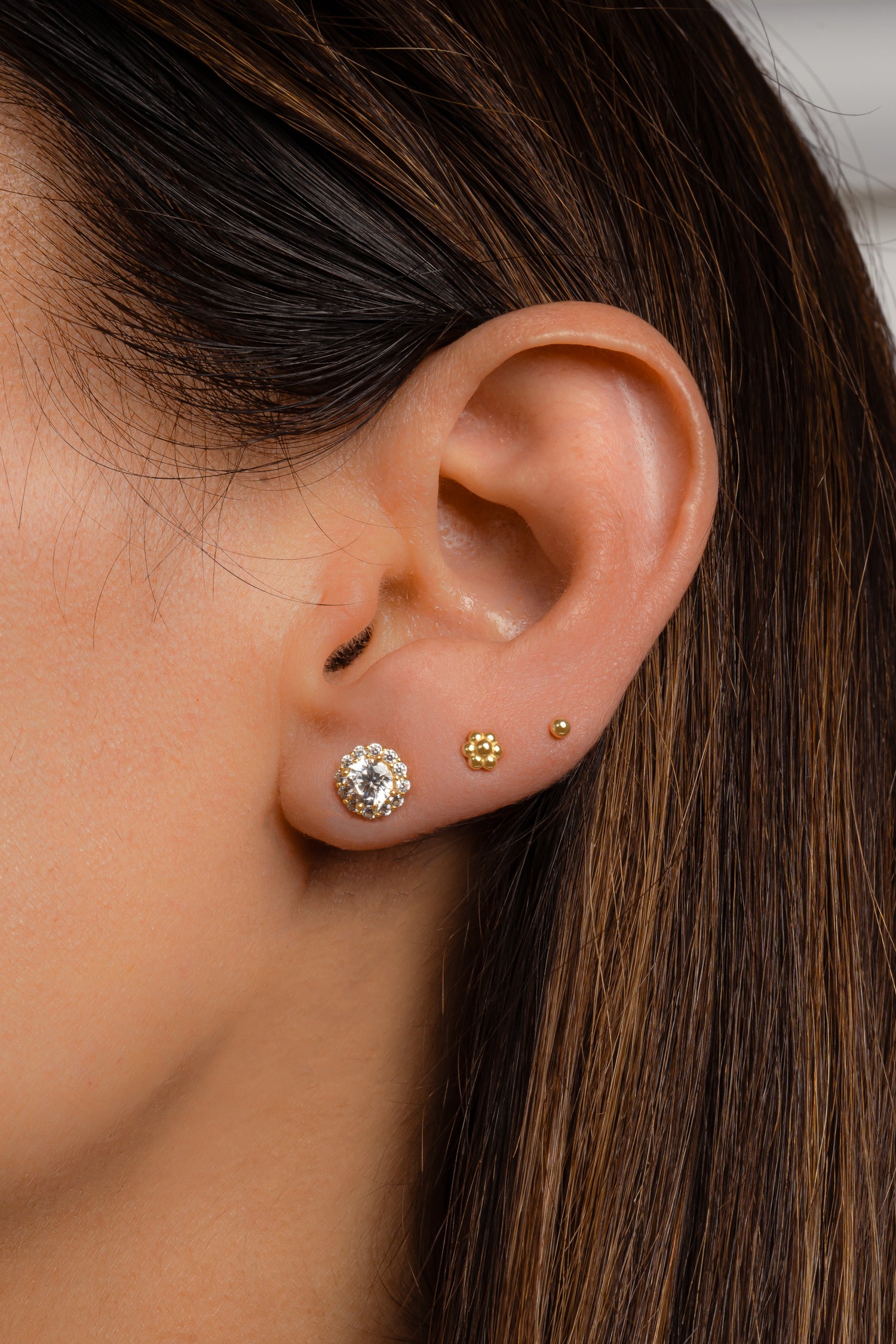 Model wearing gold halo stud earrings, a dainty gold flower stud earring, and a small ball stud earring