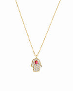 Gold necklace with a hamsa hand pendant featuring a red gemstone on a white background