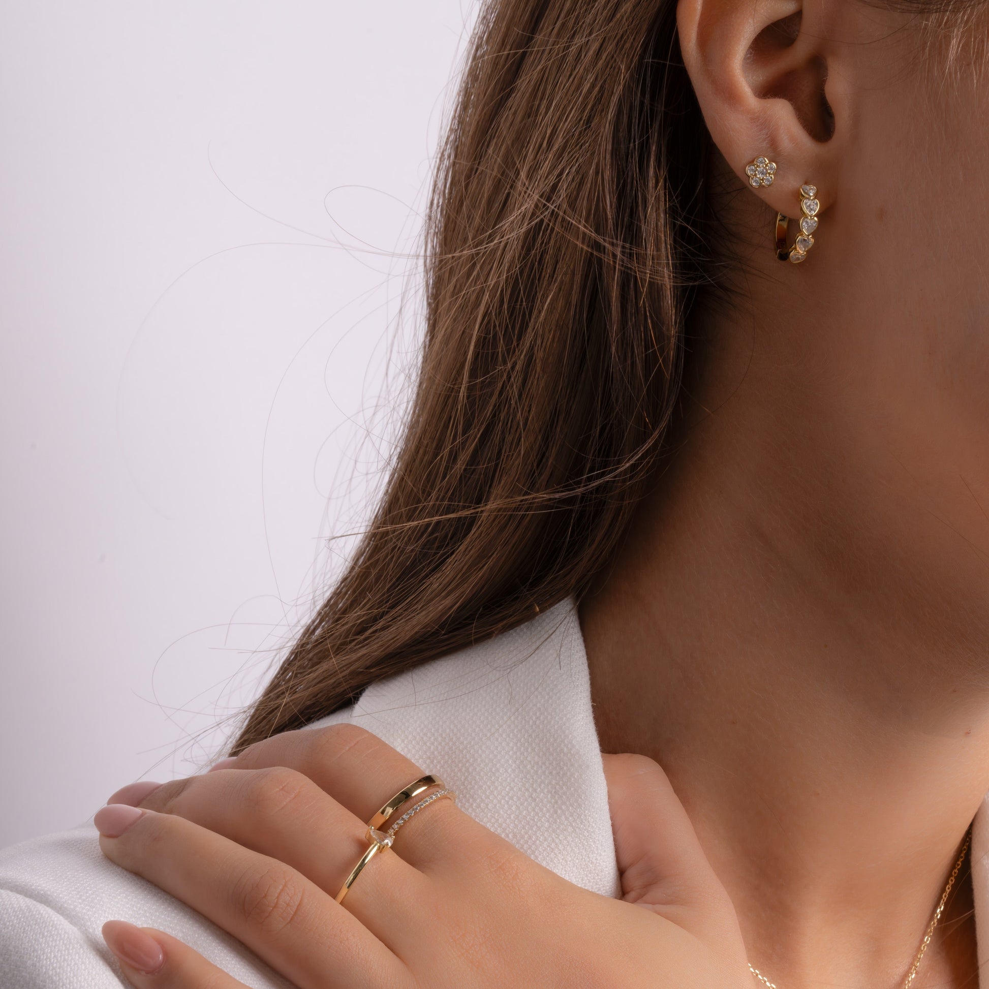 Model wearing small heart hoop earrings and diamond stud earrings paired with gold bands.