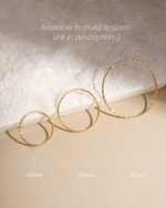 Three gold hoop earrings in different sizes on a textured surface with measurements indicated.