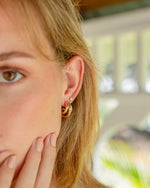 Close-up of a model wearing gold triple hoop earrings with a blurred background